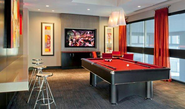 Pool table with bar seating. Wood accent wall with orange painting and accents. Large windows and tv